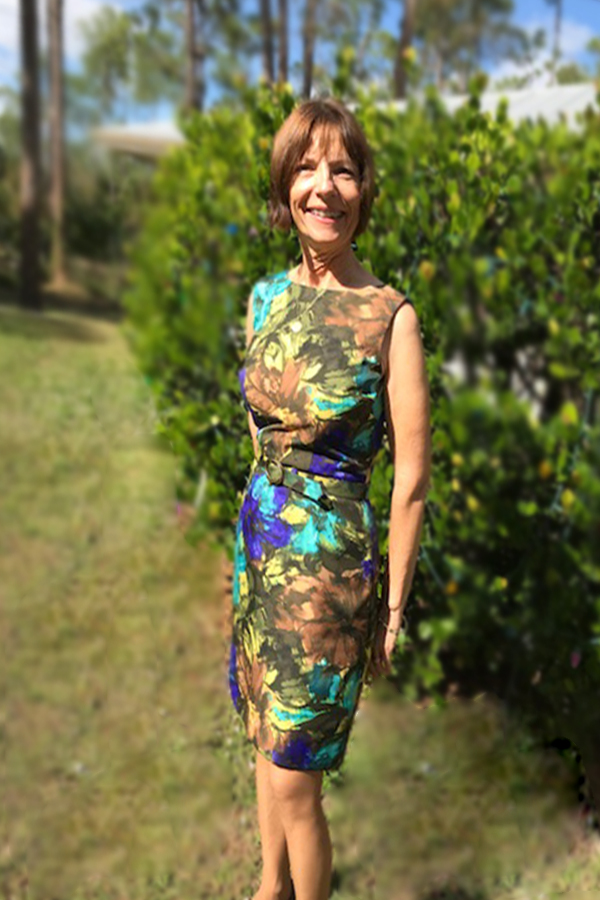 Susan Mann standing outside in front of a hedge in a multicolored dress